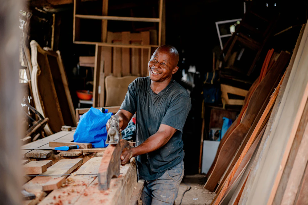 Un menuisier souriant rabote une planche dans son atelier
