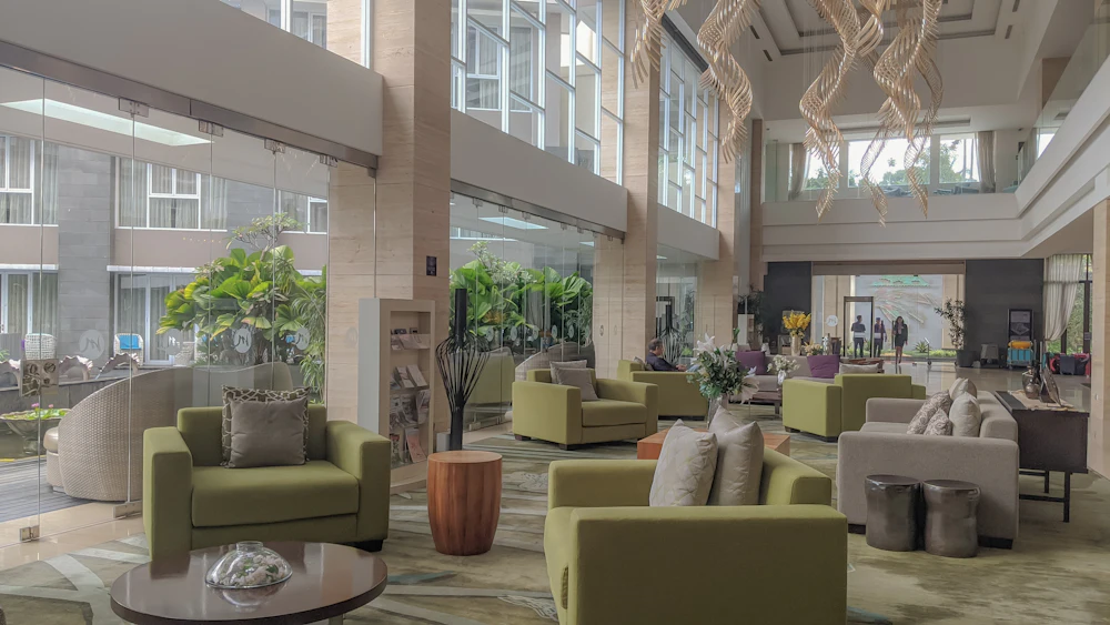 Lobby d'hôtel lumineux avec fauteuils verts et plantes